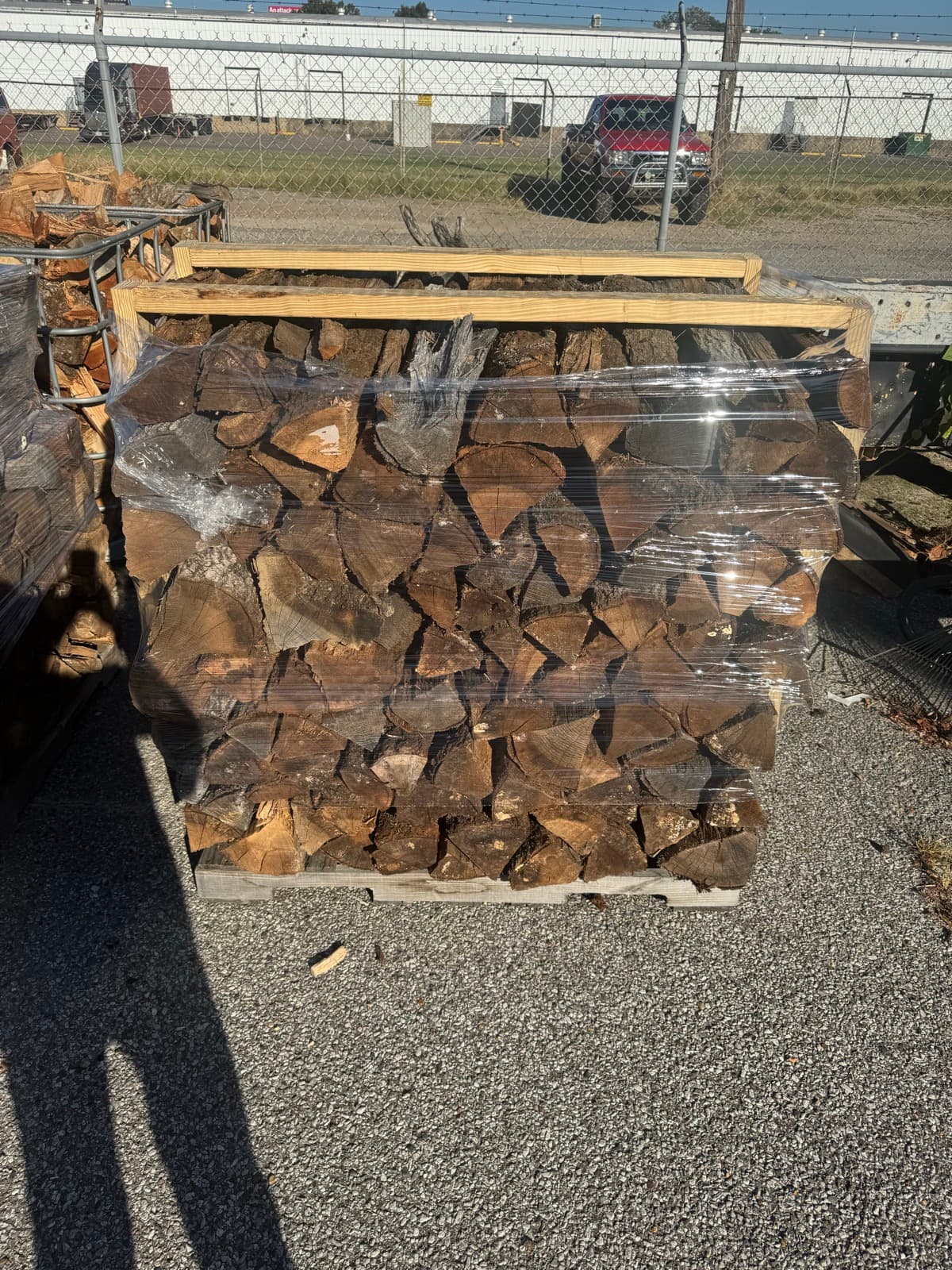 A pallet of split seasoned firewood, shrink-wrapped clear with timber battens laid across the top, standing on the gravel at the Robinson Tree yard