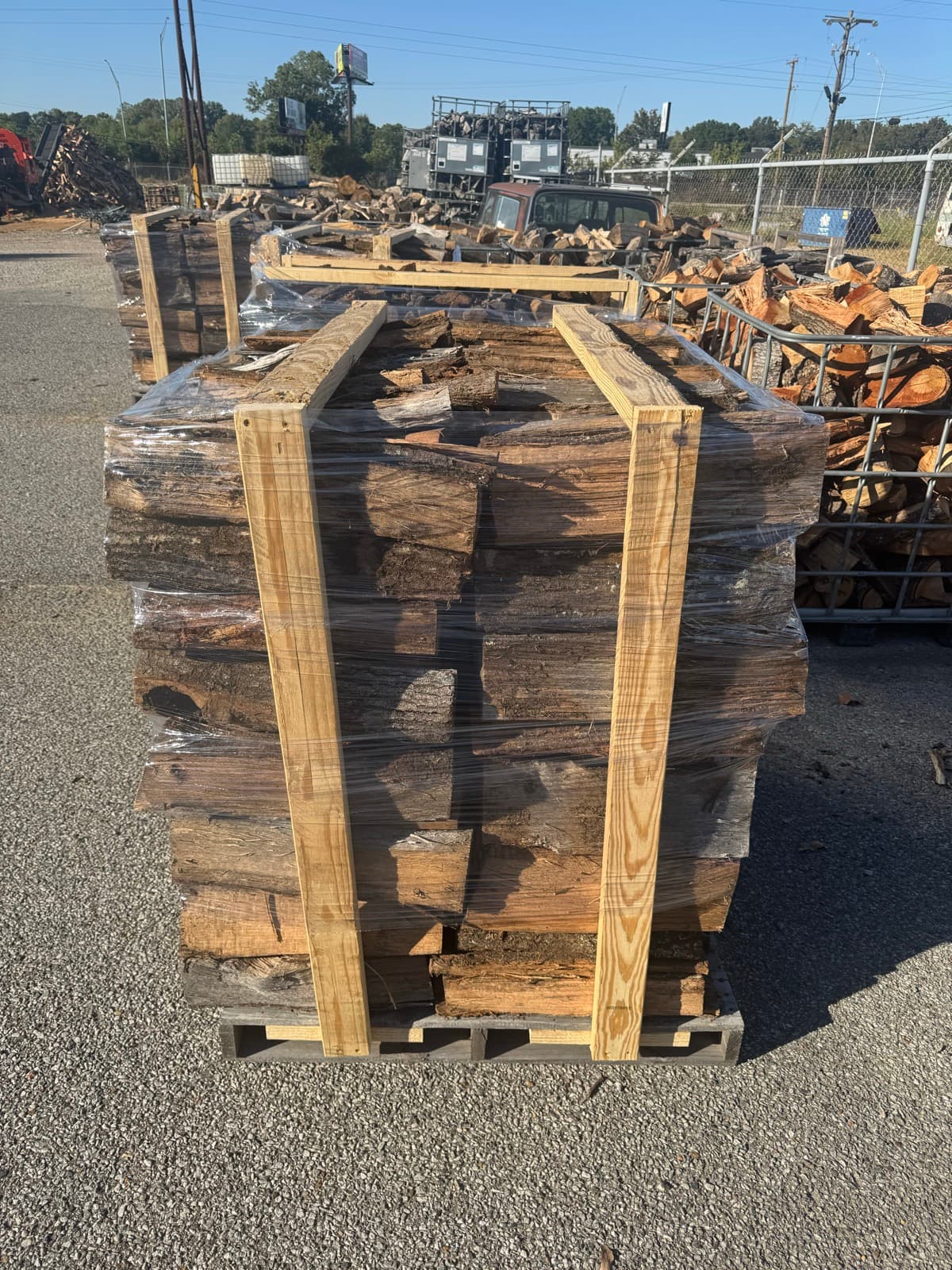 Several wrapped pallets of split firewood lined up at the Robinson Tree yard, with loose split wood stacked in metal baskets alongside
